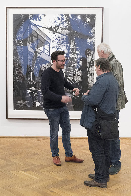 Claas Gutsche im Gespräch, im Hintergrund ein Linolschnitt des Künstlers, Foto: Etienne Dietzel