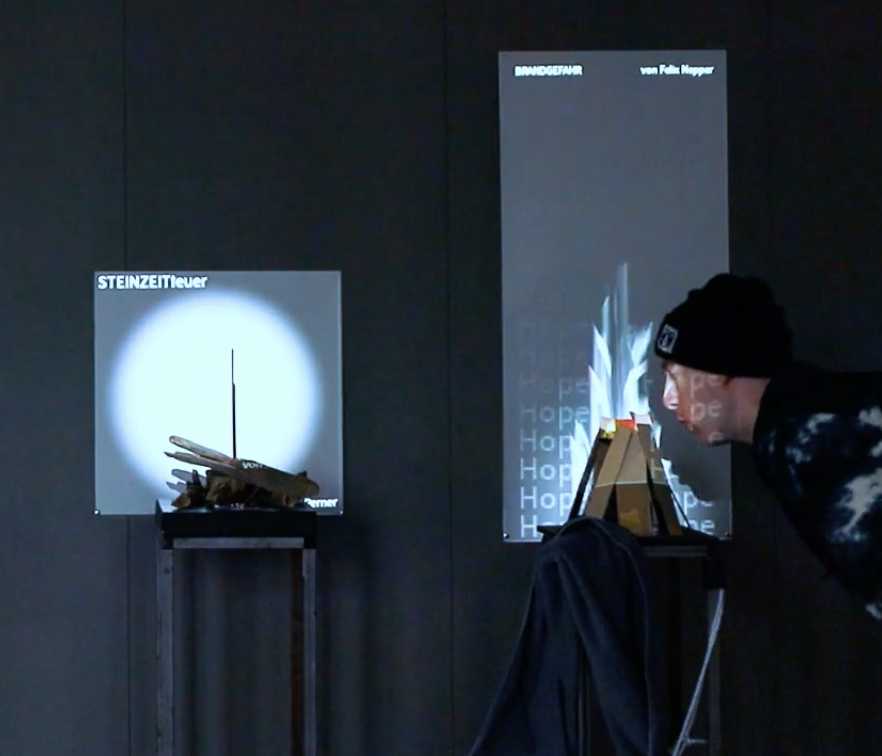 In zwei Installationen werden analoge Objekte mitteles einer Projektion an der Wand augmentiert. Ein Mensch interagiert mit einer der Installationen in dem er in einen Holzhaufen pustet. In der Projektion wird ein Feuer angefacht.  