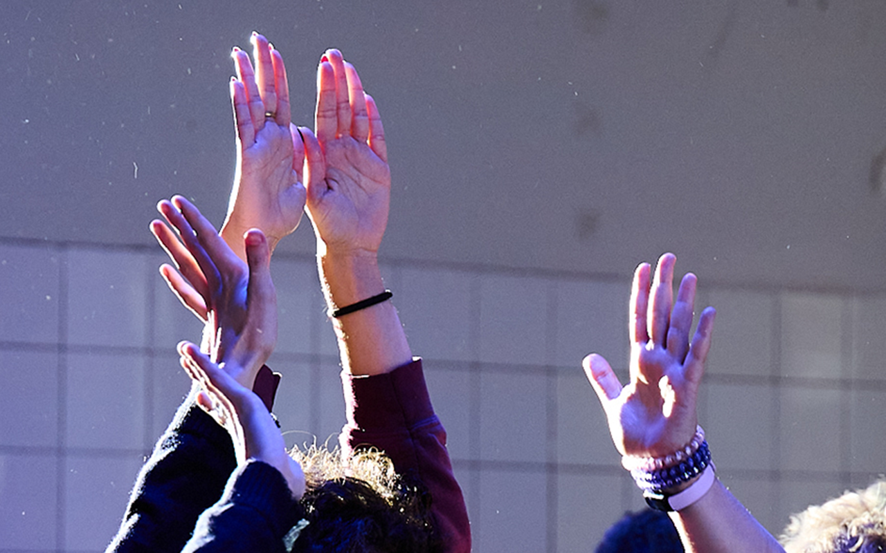  A photo of three people in a studio raising their hands into the air. Light meets fingerstips, dust particles dance. What can’t be seen in the photo is that the people are touching an imaginary object that tingles between their hands.