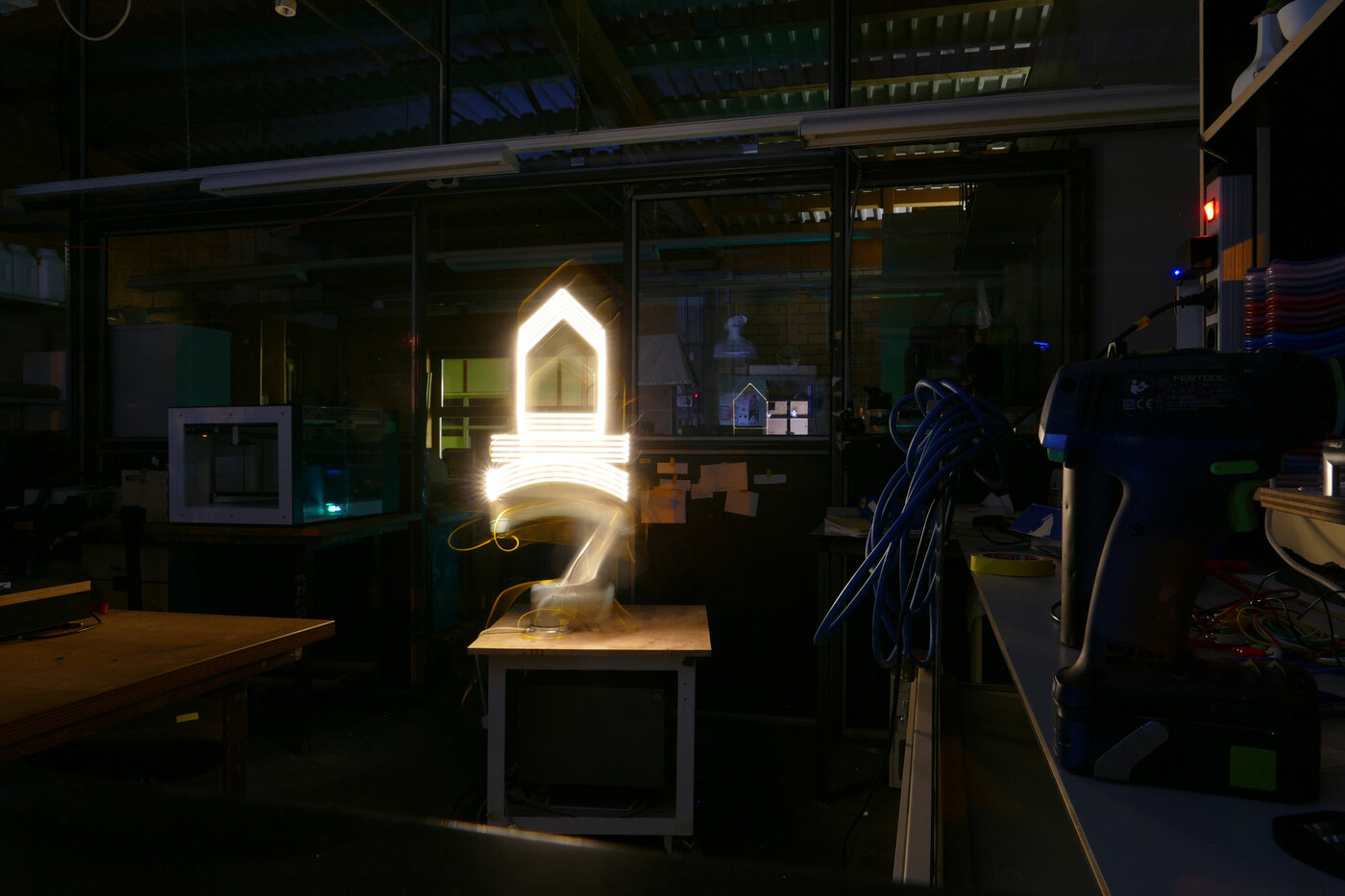 Langzeotbelichtugn von einer Lightpainting Session am Roboter. Der Roboter zeichnet mit einem LED-Streifen in einem dunklen Raum das Burg-Logo in die Luft. - Foto Simon Krautheim