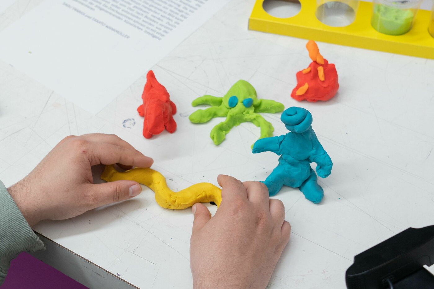 Auf diesem Bild sind kleine Knetfiguren abgebildet. Hände formen eine weitere Knetfigur.