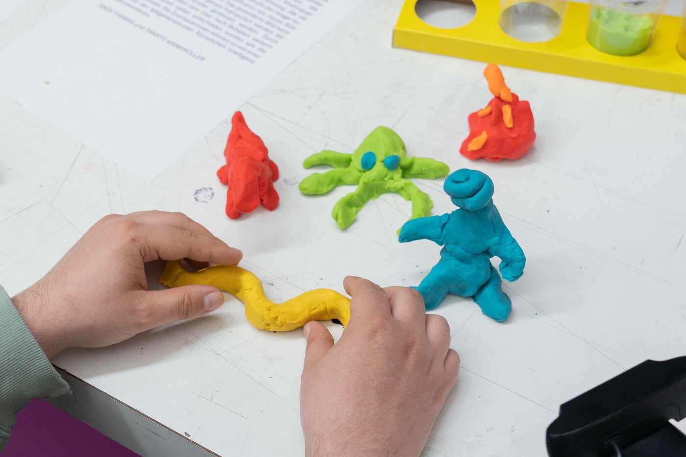 Auf diesem Bild sind kleine Knetfiguren abgebildet. Hände formen eine weitere Knetfigur.