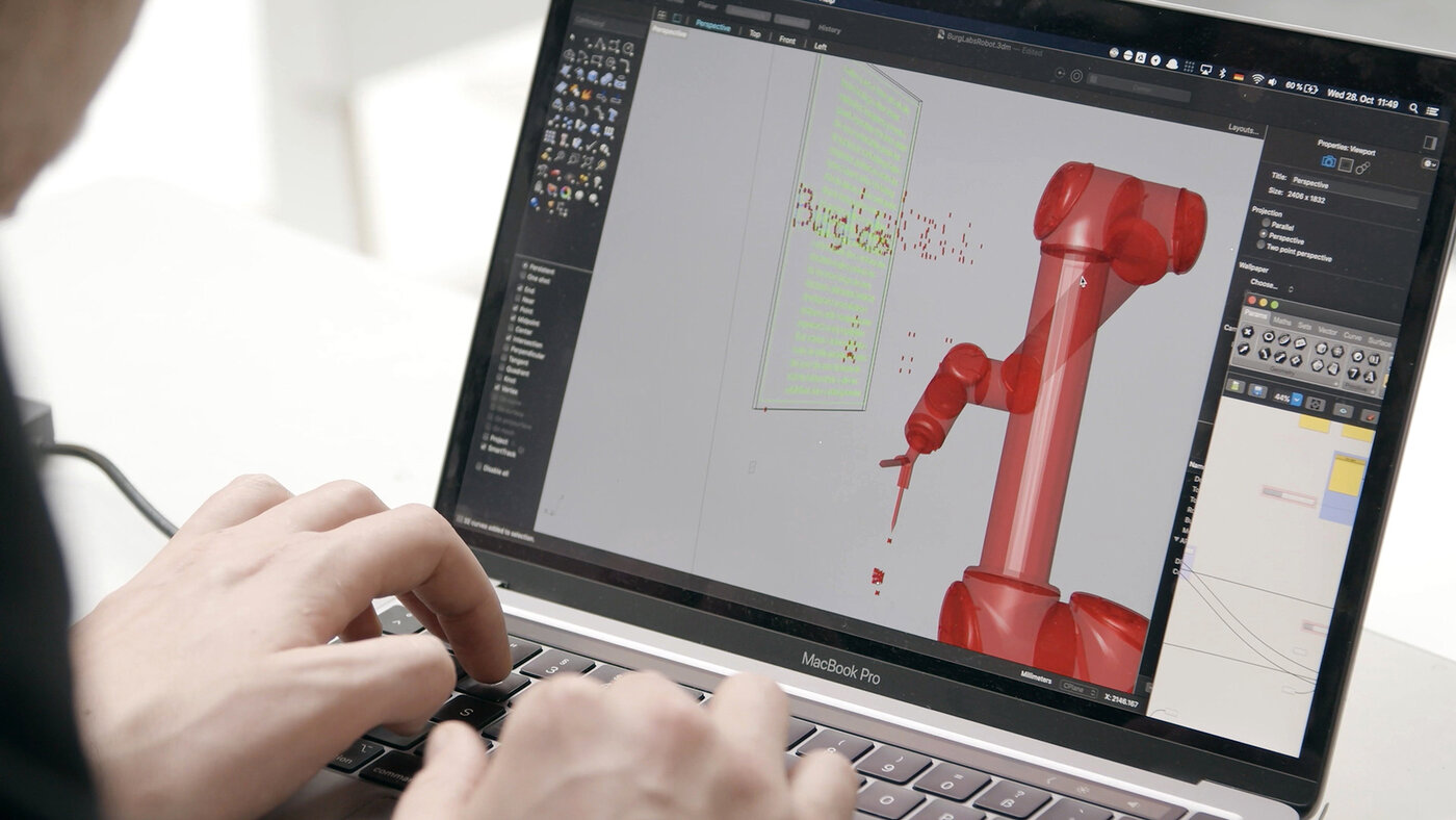 Nahaufnahme von einem Bildschirm auf dem eine 3D-Darstellung eines Roboterarms zu sehen ist. Darunter Hände die den Laptop bedienen - Foto BurgLabs