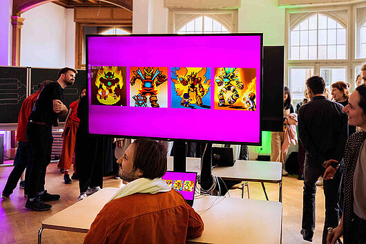 Zu sehen ist ein großer Display mit vier von einer KI erzeugten Variationen eines Comic Kampfroboters. Menschen stehen um den Display herum und betrachten das Bild.  