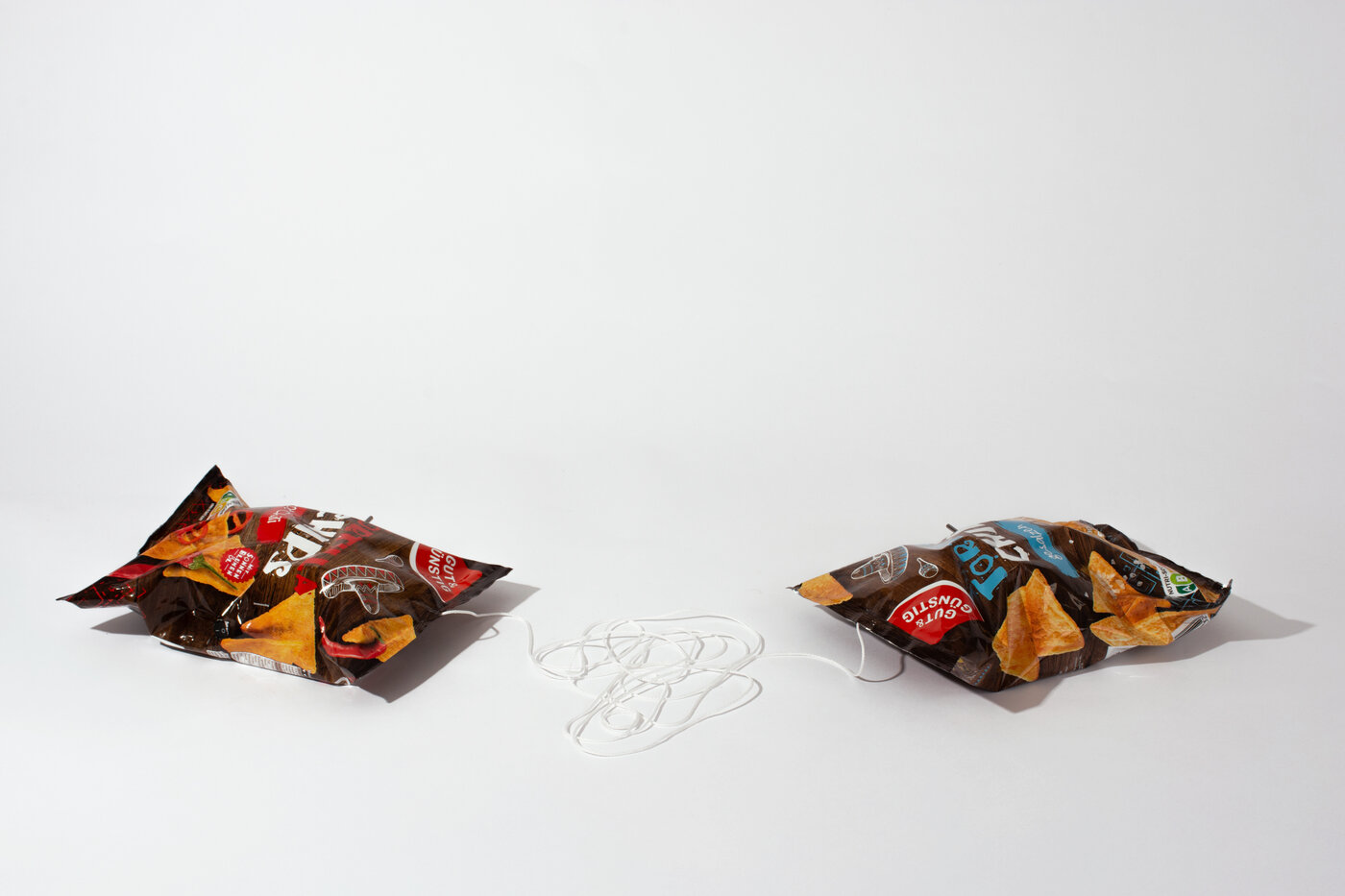 Gegenüber einander befinden sich zwei Chipstüten, beide haben jeweils das Ende einer Schnur im „Mund“, welche zwischen ihnen als Knäuel liegt. Man sieht, dass sich in den Chipstüten etwas befindet, wobei es sich um eine Mechanik handelt.