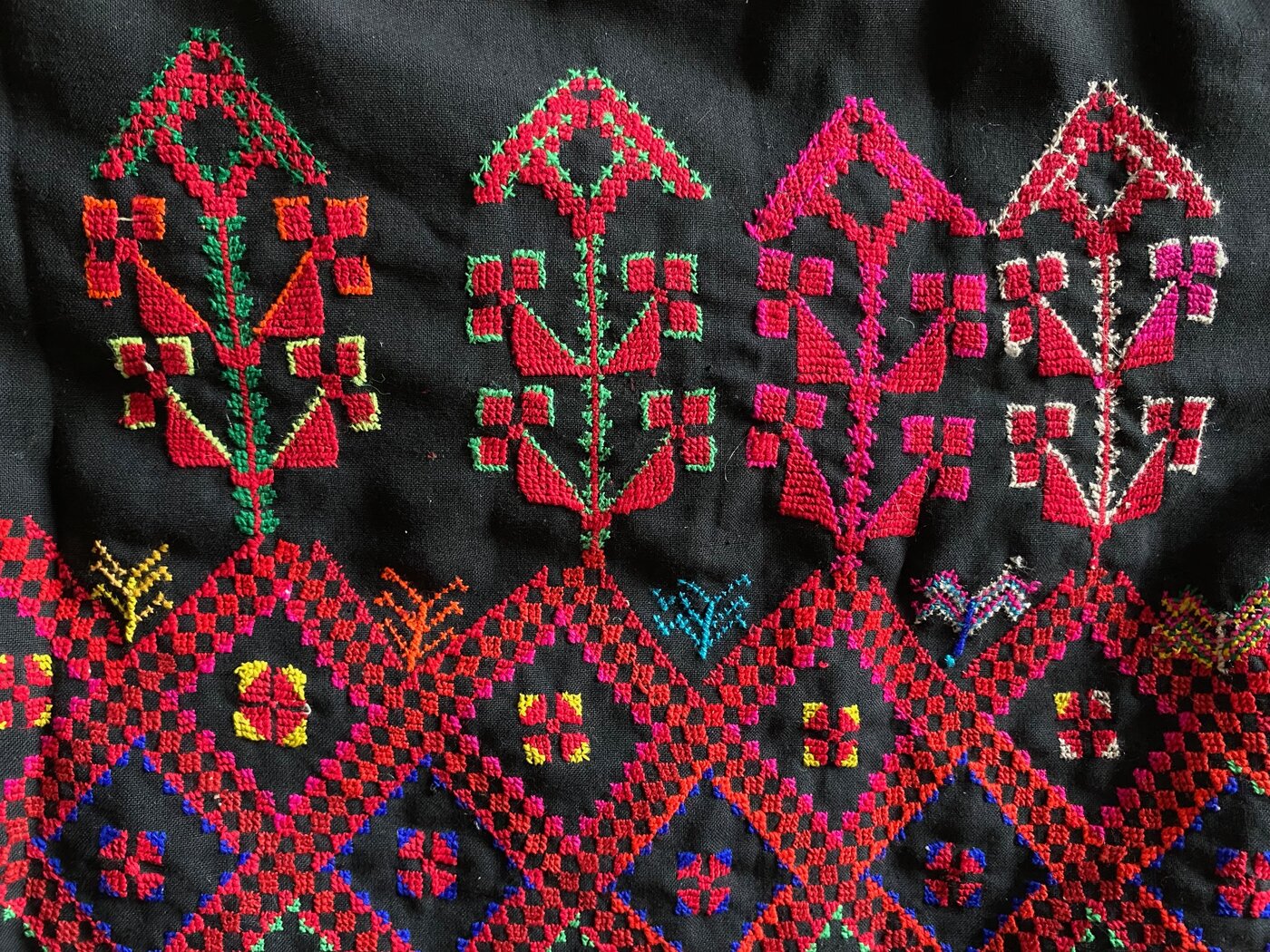 Farbfoto eines Ausschnitts einer schwarzen textilen Fläche mit quadratisch-geometrischen ornamentalen Mustern in Rottönen mit blauen, grünen und gelben Farbakzenten