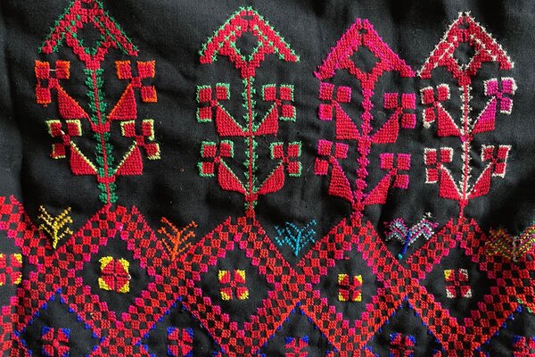 Farbfoto eines Ausschnitts einer schwarzen textilen Fläche mit quadratisch-geometrischen ornamentalen Mustern in Rottönen mit blauen, grünen und gelben Farbakzenten