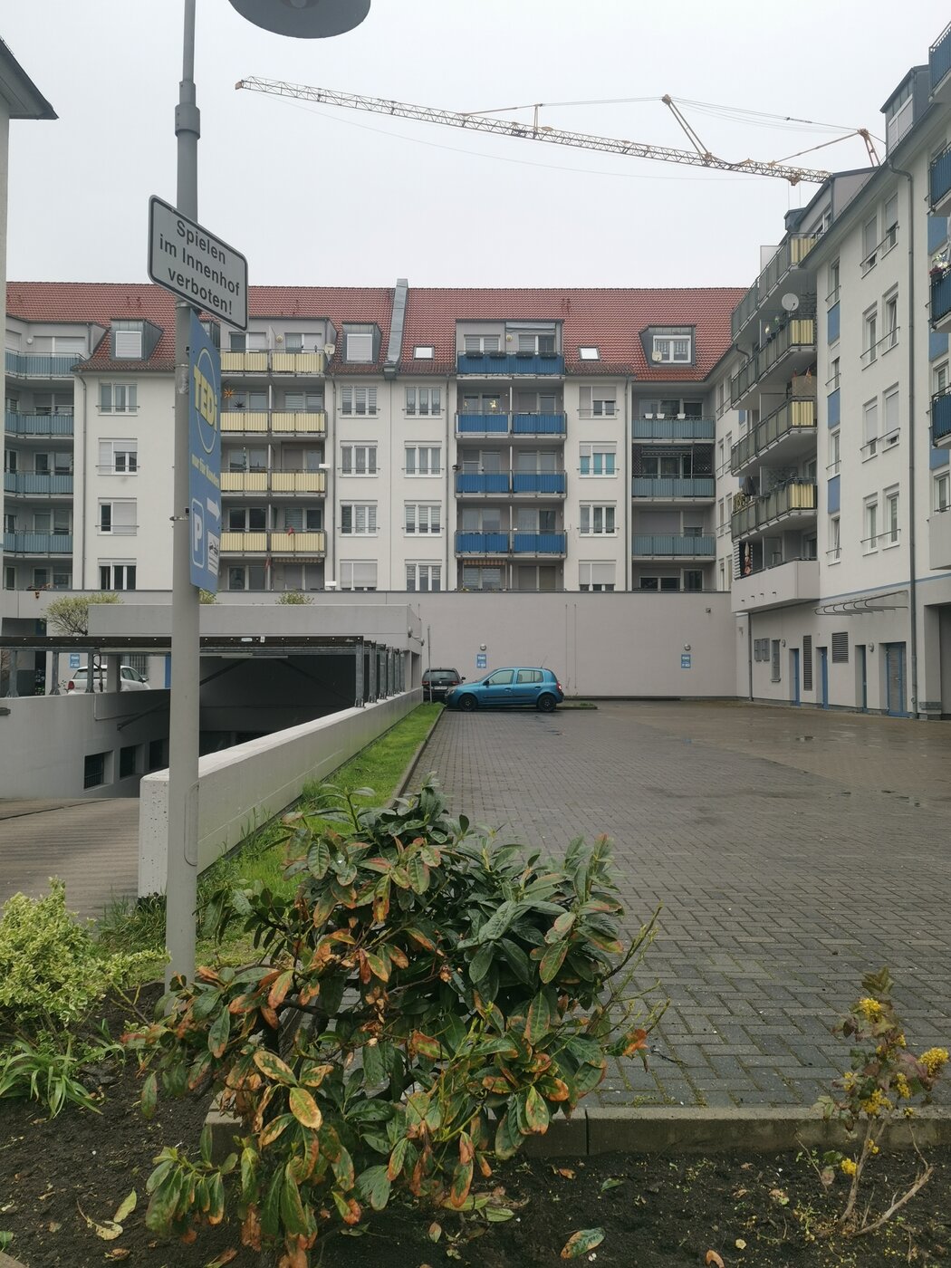 Auf dem Bild ist ein trister gepflasterter Innenhof zwischen mehrstöckigen Häusern zu sehen. Ein Auto ist dort geparkt. Links im Bild ist ein Schild zu erkennen auf dem "Spielen verboten" steht.