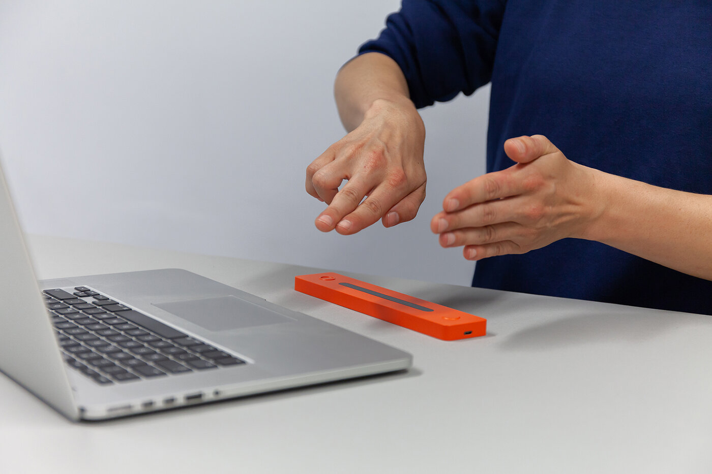 ein orange-farbiger kleiner viereckiger Sensor vor einem Laptop, der im Bild durch den Sensor mit Handgesten gesteuert wird