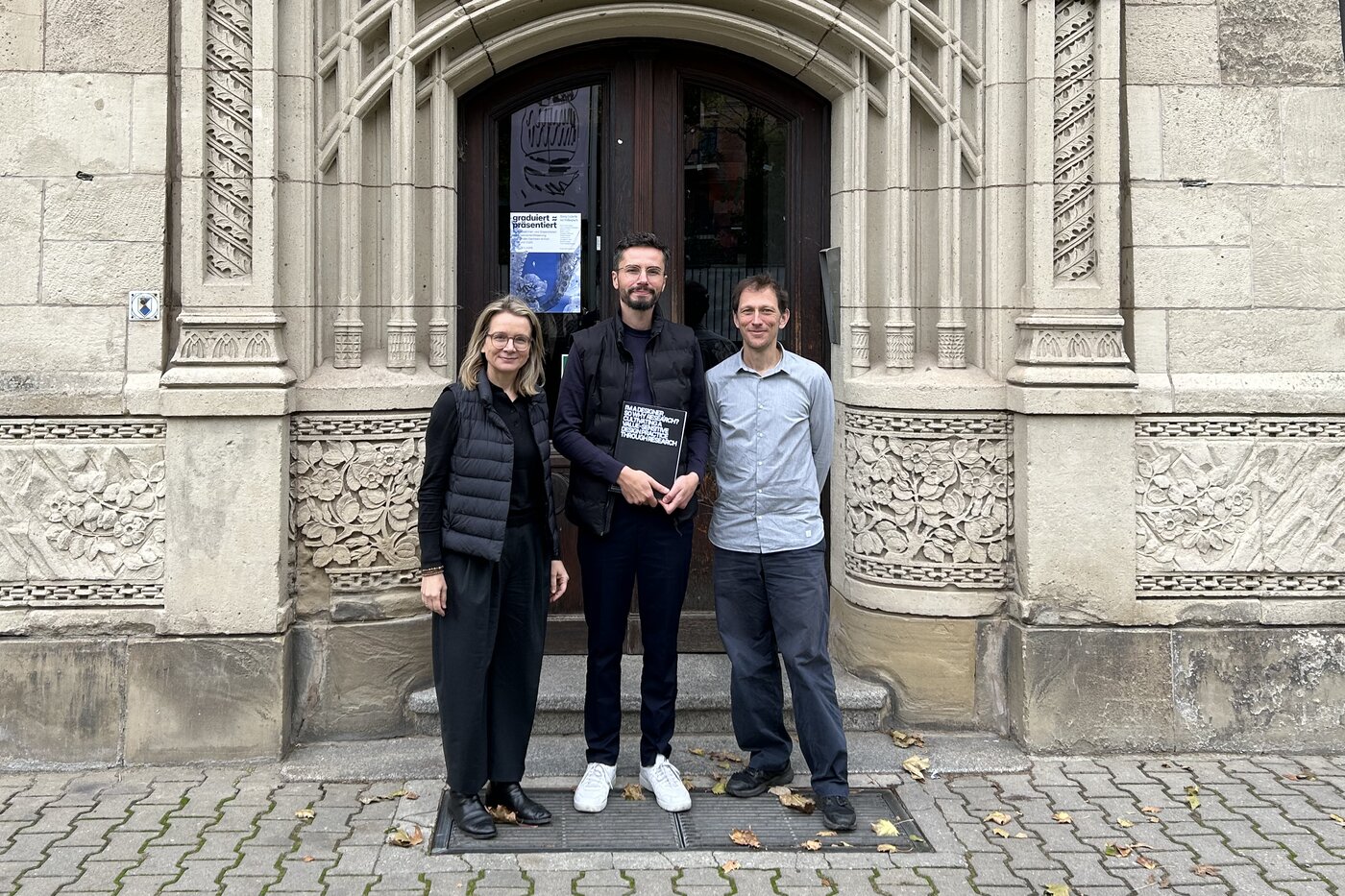Peter Sörries steht nach der erfolgreichen Verteidigung seiner Dissertation mit Prof. Dr. Claudia Müller-Birn und Prof. Dr. Pablo Abend vor dem Haupteingang der BURG