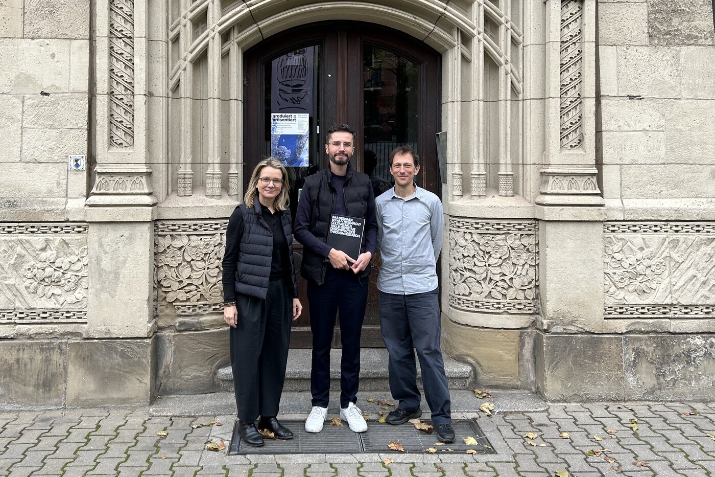 Peter Sörries steht nach der erfolgreichen Verteidigung seiner Dissertation mit Prof. Dr. Claudia Müller-Birn und Prof. Dr. Pablo Abend vor dem Haupteingang der BURG