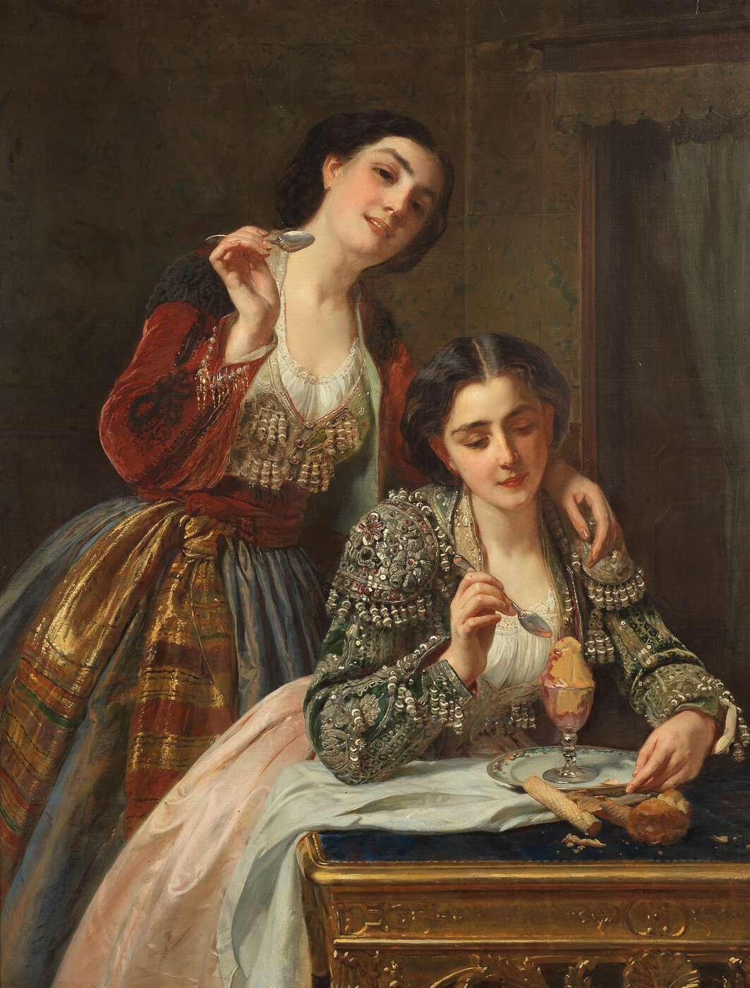 Zu sehen sind zwei braunhaarige Frauen. Eine sitzt am Tisch, vor ihr steht ein Dessert in einem eleganten Glaskelch, sie hält ein Dessertlöffel in der Hand um es zu essen. Hinter ihr steht die andere Frau und hat ebenfalls ein Dessertlöffel in der Hand.