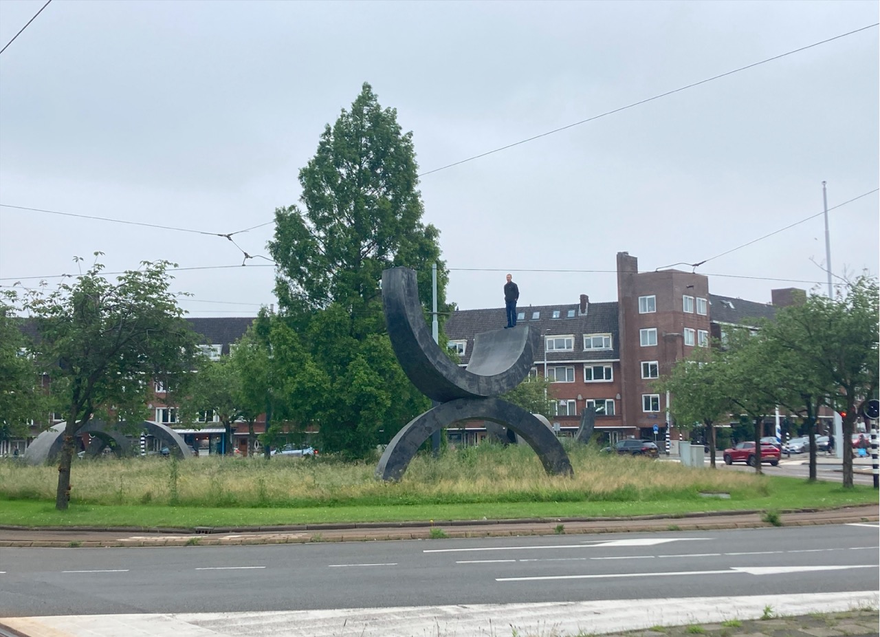 Als Dolores Martín Hidalgo mich hier fotografierte, sagte dey: Per que non giocci con la scultura? (Warum spielst du nicht mit der Skulptur?) Ich: Per me non é un gioccio. (Für mich ist es kein Spiel.) DMH: Qué tedesco, quest’opera. (Wie deutsch, diese Arbeit.) Das war das erste mal in unserer langen Zusammenarbeit und in all unseren Gesprächen, dass unsere Nationalität im Bezug auf meine Arbeit erwähnt wurde. Und das am “Surinameplein” in Amsterdam. (Suriname als ehemalige Kolonie der Niederlande) Das hat mich wirklich zum Nachdenken angeregt: Mein Umgang scheint stark von der vermeintlichen Neutralität oder zumindest analytischer Sterilität und Geplantheit von Personen wie Gregor Schneider oder Wermke und Leinkauf geprägt zu sein. Bei all meiner Abneigung gegenüber dem nationalistischen Konstrukt habe ich wohl die volle männliche deutsche Kunstriegen-Logik abbekommen?
André Theo Aart, Volten‘s Skulptur, Surinameplein, Amsterdam 2024 Foto: Dolores Martín Hidalgo