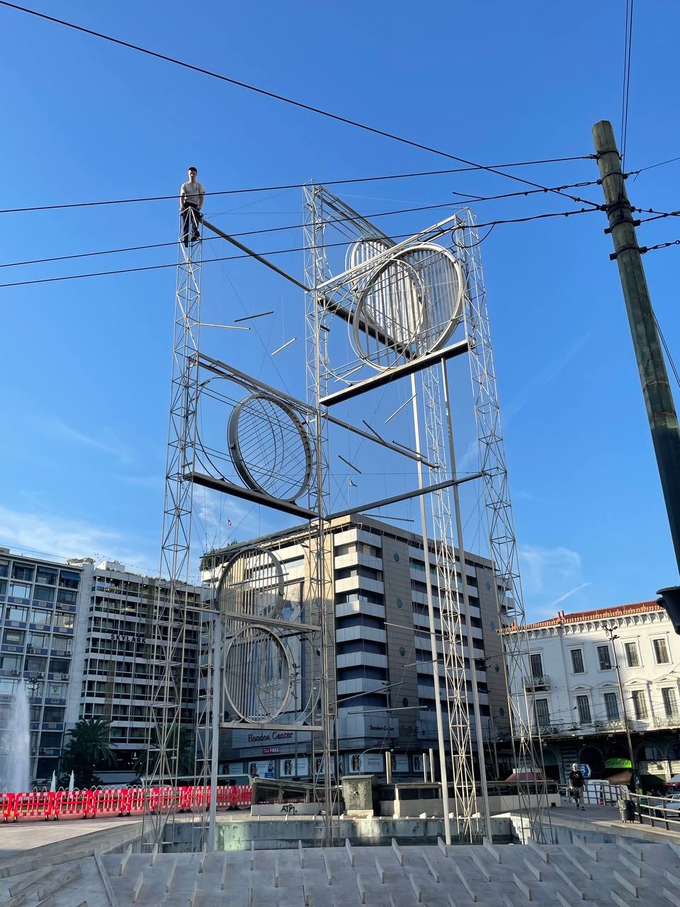 Die erste Statue, auf die ich für dieses Projekt klettern wollte und die Letzte, bei dir ich es geschafft habe. Danach zittern meine Knie und mein Bein hat sich so verkrampft, dass ich es noch tagelang spüre. Absurderweise ist die Reaktion gelinde gesagt verhalten: An diesem Hauptverkehrsknotenpunkt von Athens Straßen, U-Bahnen, Bussen und Geschichte, dem „Platz der Weisheit“ interessiert sich natürlich niemand für einen weiteren deutschen Touristen, der sich irgendwie daneben benimmt. Die ersten Male, als ich hier 2023 wie 2024 mit dieser Absicht stand, habe ich mich nicht getraut, weil die Polizei über den Platz patrouillierte. Im Nachhinein frage ich mich, ob sie mein Krisenexperiment überhaupt bemerkt hätten. Platia Omonias, Athen, 2024, Foto: Nik Haberstock